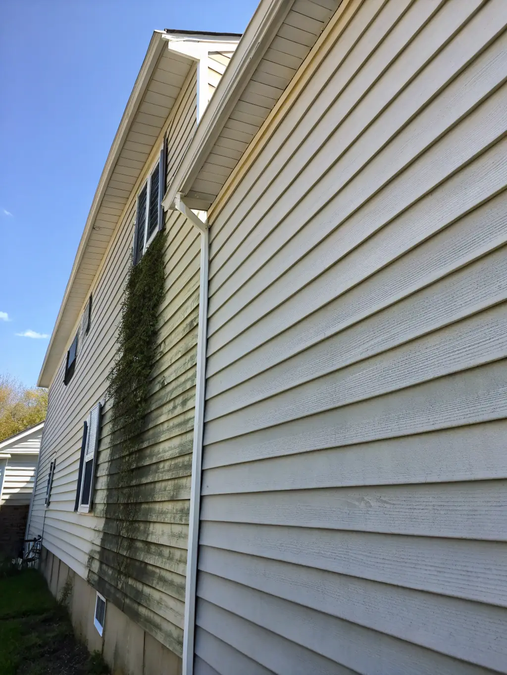 A residential house with siding being power washed, showcasing the cleaning process and the immediate difference in appearance.